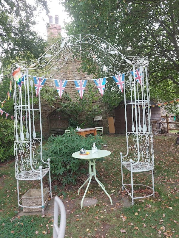 A quaint garden setting with a decorative gazebo, Union Jack bunting, and a small green table with chairs.