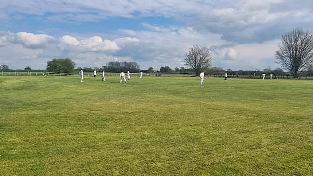Cricket players in white uniforms on a green field under a blue sky with scattered clouds in Little Ribston, Yorkshire.