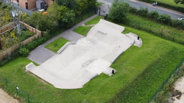 Aerial view of Thirsk Skatepark featuring concrete ramps, green grass, and nearby trees along a road.