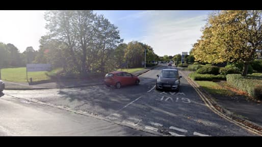 Car park entrance in Edenthorpe, Yorkshire, with trees and parked cars along a winding road.