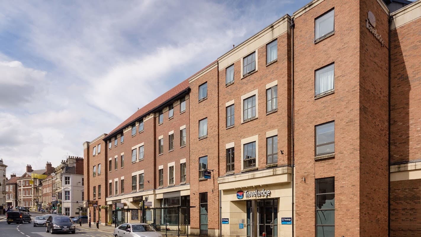 Modern brick hotel building with large windows, featuring the Travelodge sign, set against a cloudy sky.