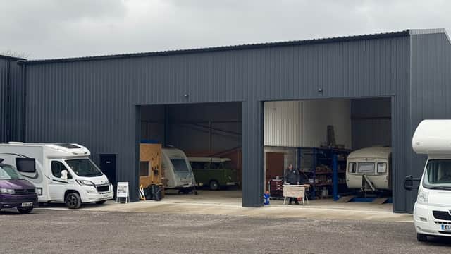 Gray workshop with two large openings, caravans outside, and a person working on a vehicle in the entrance.
