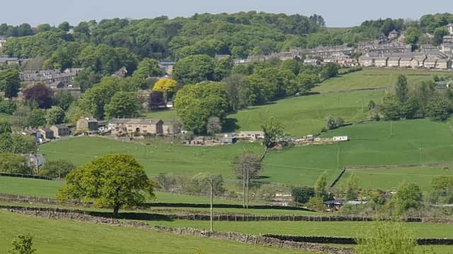 Lush green hills and fields surround Cross Roads Park, with quaint stone buildings and trees dotting the landscape.