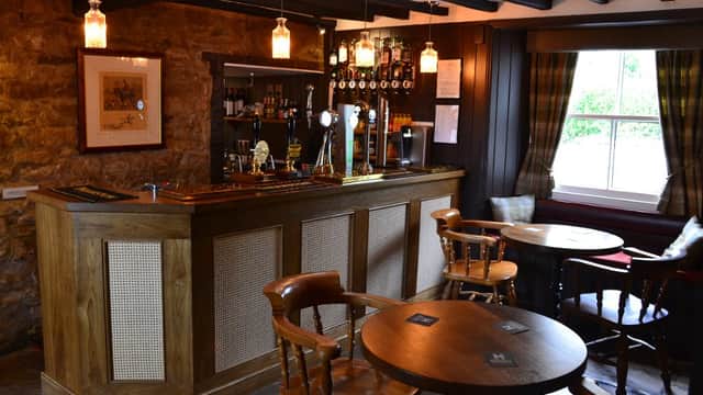 Cozy bar interior with wooden furniture, a stone wall, and shelves lined with various spirits and drinks.