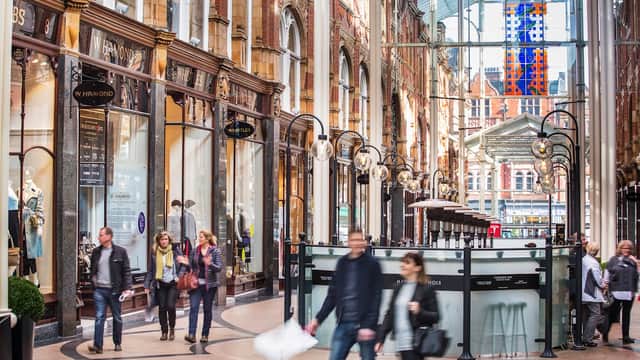 Victorian-style shopping arcade with glass roof, ornate architecture, and shoppers walking through the bustling space.