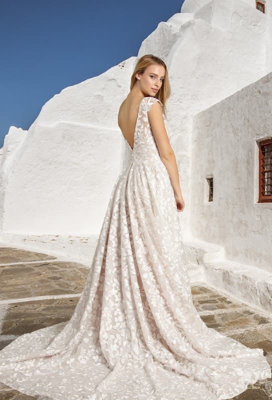 A model wearing a stunning backless wedding dress with floral patterns, standing against a whitewashed building.