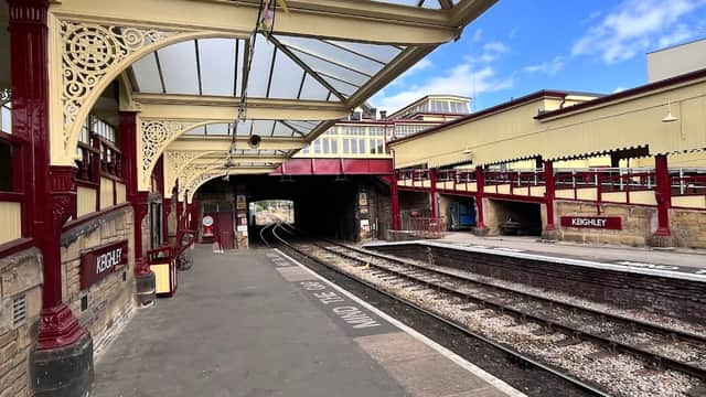 Keighley Station features ornate red and yellow architecture, platform tracks, and a clear blue sky above.