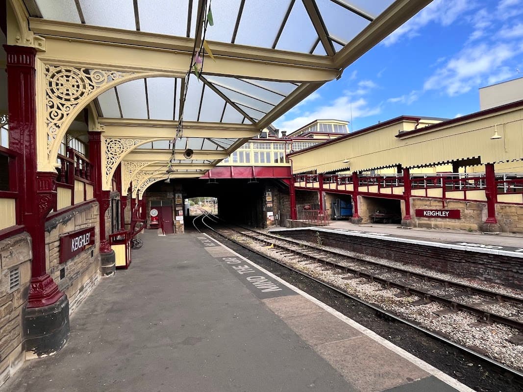 Keighley Station features ornate red and yellow architecture, platform tracks, and a clear blue sky above.