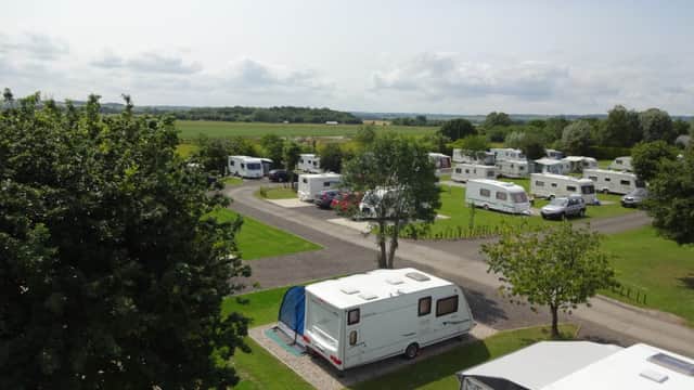 Caravans and motorhomes parked on a grassy campsite with trees and open fields in the background.