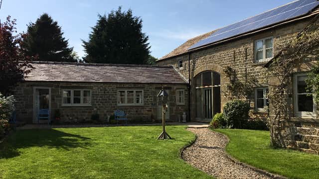 Charming stone cottage with solar panels, surrounded by lush greenery and a gravel path in Kirkby Malzeard, Yorkshire.