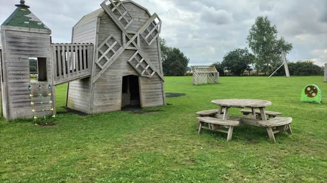 Wooden playground structure resembling a windmill, picnic table, and green grass under a cloudy sky.