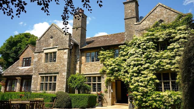 Historic stone building with ivy-covered walls, surrounded by greenery and outdoor seating in a tranquil setting.