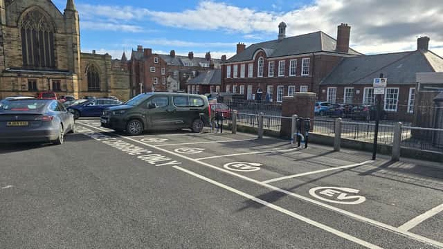 Connected Kerb Charging Station in a parking area with EV signage, near buildings and a church in Whitby, Yorkshire.