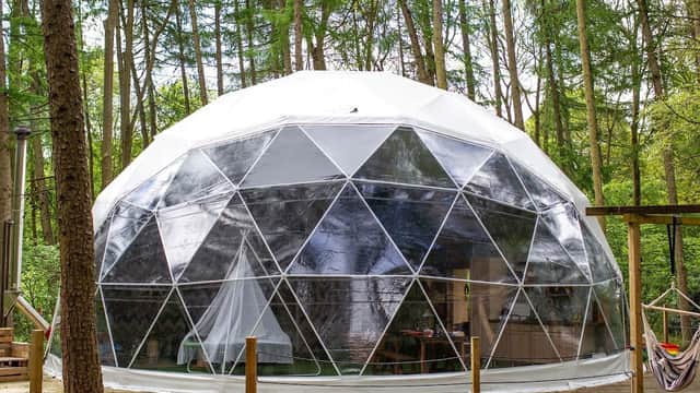 Geodesic dome glamping structure surrounded by trees at Camp Kátur in North Yorkshire, with a wooden deck.