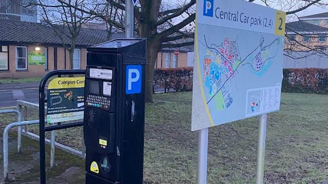 Pay & Display parking meter beside a sign for Central Car Park, with a map and directional arrow in Heslington, Yorkshire.