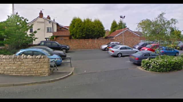 Pay & Display parking area in Sherburn in Elmet, with cars parked and greenery surrounding a stone wall.