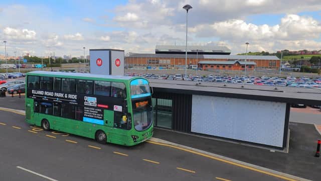 Green bus at Elland Road Park & Ride, with a large parking lot and a stadium in the background under a cloudy sky.