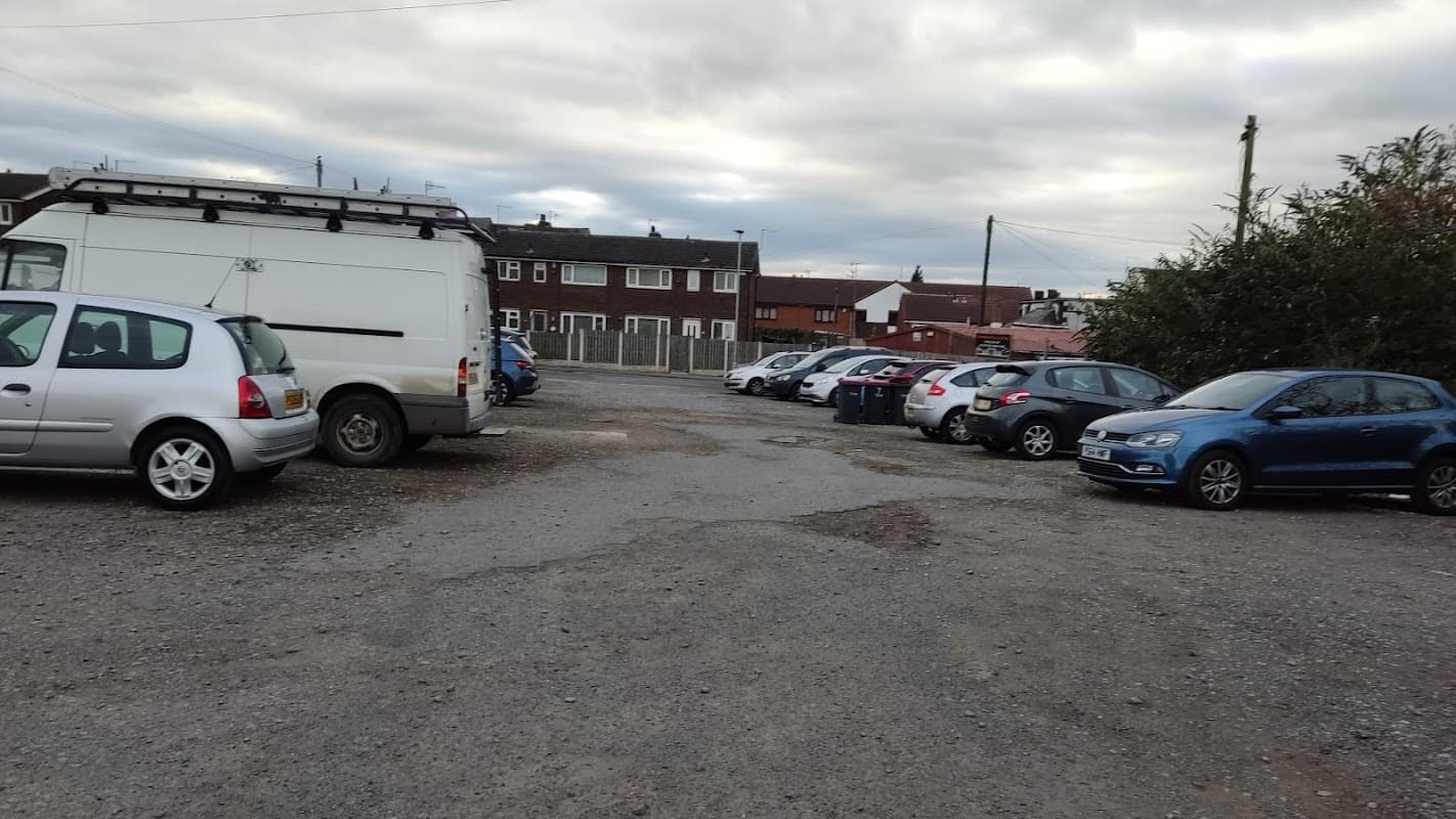 Gravel car park with parked cars, buildings in the background, and a cloudy sky over Rotherham, Yorkshire.