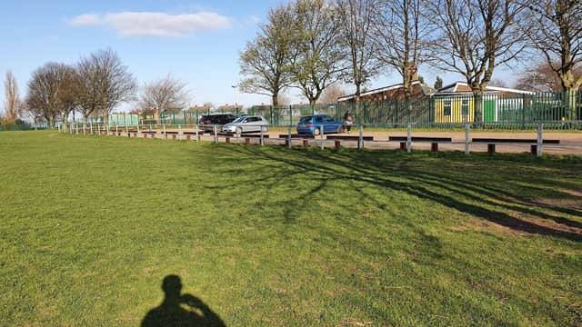 Car park in Pontefract with parked cars, green grass, trees, and a person walking along a path.