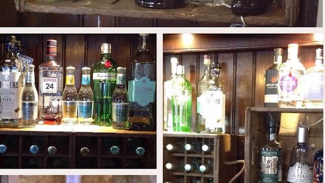 A rustic bar display featuring various gin bottles, mixers, and glassware against a wooden backdrop.