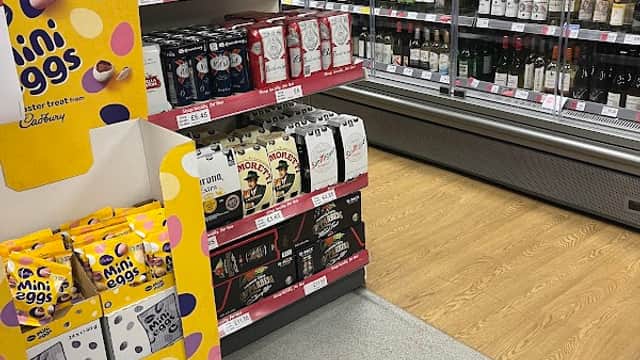 Shelves stocked with wine and beer, featuring a display of Cadbury mini eggs in a corner shop setting.