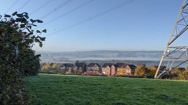 View of residential buildings in Aston, Yorkshire, with misty hills and power lines in the background.