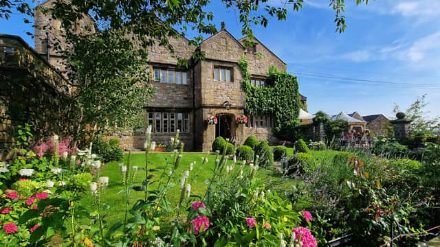 Historic Stirk House Hotel surrounded by lush gardens and colorful flowers under a clear blue sky.