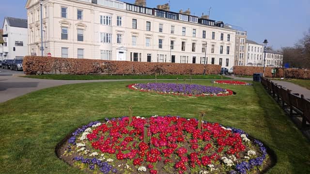 Crescent Gardens features vibrant flower beds in circular patterns, surrounded by a manicured lawn and historic buildings.