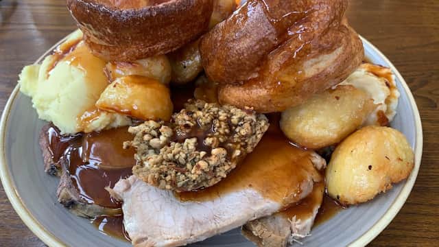A hearty plate featuring roast beef, Yorkshire puddings, roast potatoes, mashed potatoes, and rich gravy.