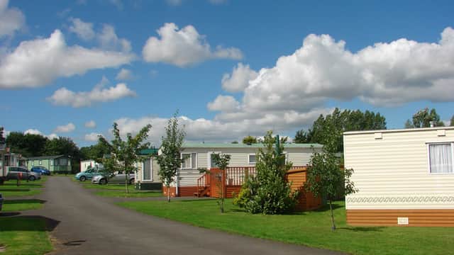 Caravan park with neatly arranged mobile homes, green lawns, trees, and a blue sky dotted with fluffy clouds.