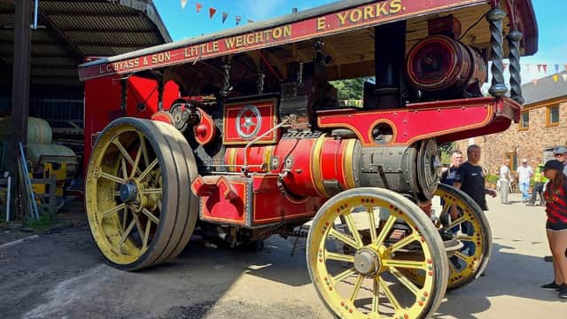Vintage steam engine with bright red and yellow detailing, set against a backdrop of bunting and onlookers at a rally.