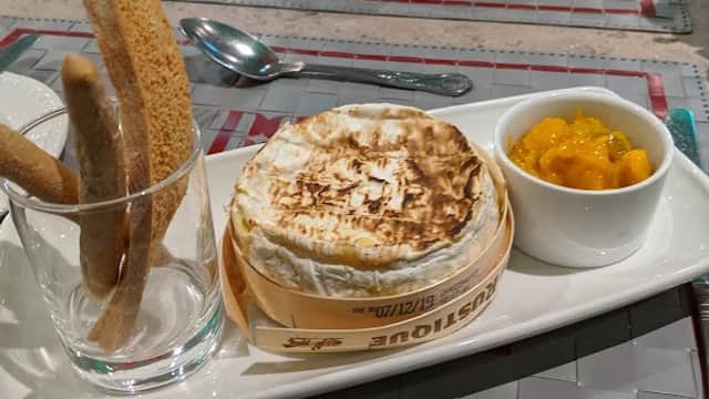 A plate featuring baked cheese, mango chutney, and breadsticks, set on a stylish table at Bollywood Brasserie.