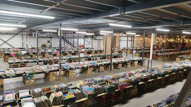 A spacious bookshop with rows of wooden crates filled with colorful books, under industrial-style lighting.