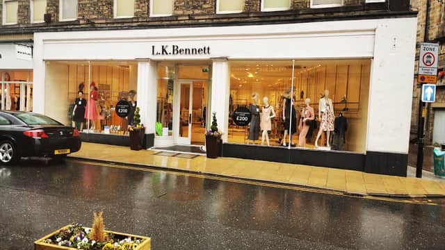 L.K. Bennett storefront with large windows displaying colorful clothing, mannequins, and a rainy street scene.