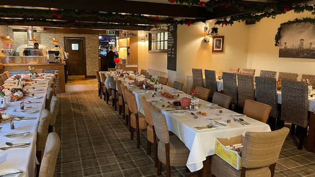Dining area with neatly set tables, wooden beams, festive decorations, and a view of the kitchen in the background.