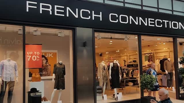 French Connection storefront with large signage, showcasing clothing displays and a customer seated nearby.