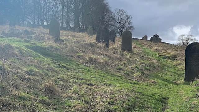 Grassy slope with gravestones, surrounded by trees under a cloudy sky.