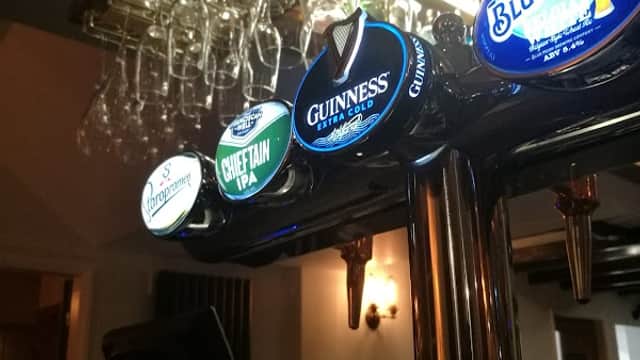 Bar counter with various beer taps, including Guinness and Chieftain IPA, and hanging glasses in the background.