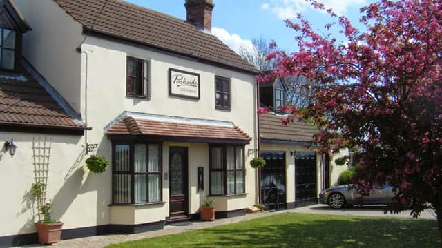 Charming two-story guest house with a sign, surrounded by greenery and blooming pink flowers in Pollington, Yorkshire.