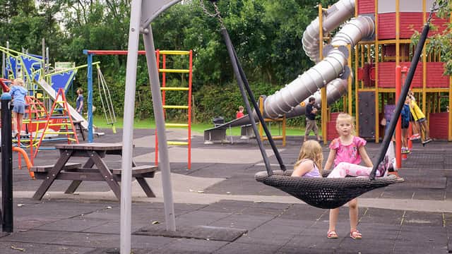 Children playing on a swing and near colorful playground equipment with a slide and climbing structures in a park setting.