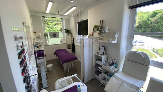 Bright beauty salon with a treatment bed, white furniture, plants, and nail polish displays in a modern setting.