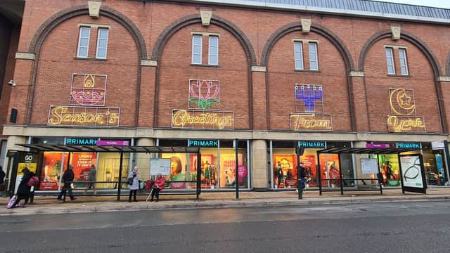 Primark storefront in Harrogate with colorful neon signs and shoppers outside, featuring large windows and brick architecture.