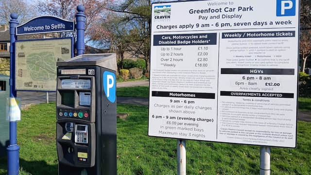 Greenfoot Car Park sign with parking rates, payment machine, and a welcome sign for Settle, surrounded by trees.