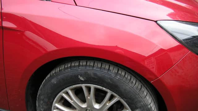 Close-up of a shiny red car's front fender and alloy wheel, showcasing smooth paint and a textured tire.