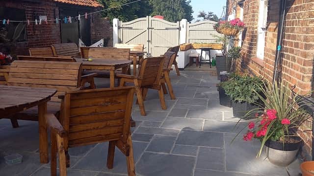 Outdoor seating area with wooden tables and chairs, stone flooring, and potted plants at The Anvil Arms in Wold Newton.
