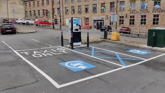 Free parking area with marked taxi spaces, electric vehicle charging station, and nearby brick buildings in Farsley.