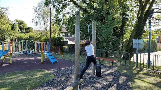 Child playing on a horizontal bar in a playground with colorful equipment and greenery in Bardsey, Yorkshire.