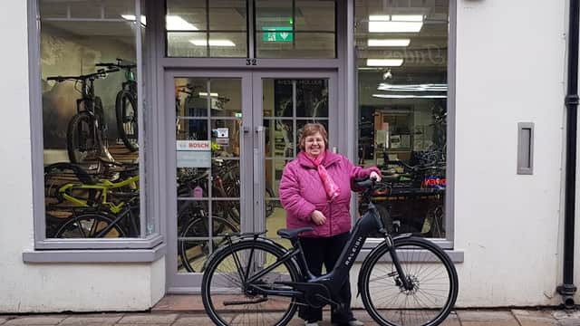 A woman in a pink jacket stands next to an electric bike outside The Electric Transport Shop in York.