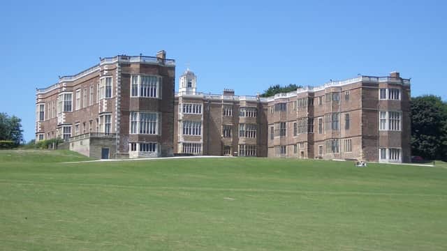 Historic brick mansion with large windows and expansive green lawn under a clear blue sky.