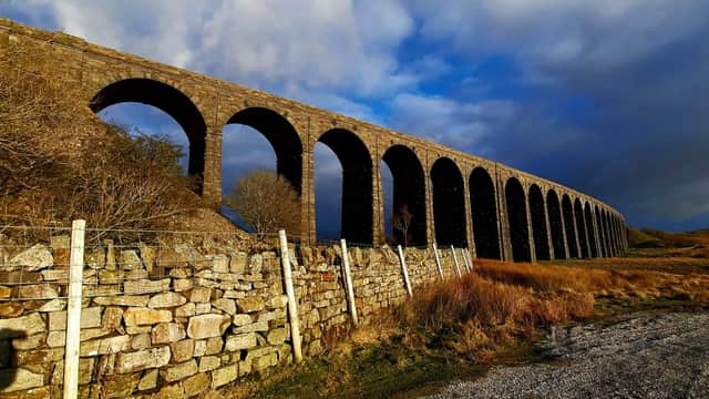 Ribblehead Viaduct arches over a grassy landscape under a dramatic sky, framed by dry stone walls.